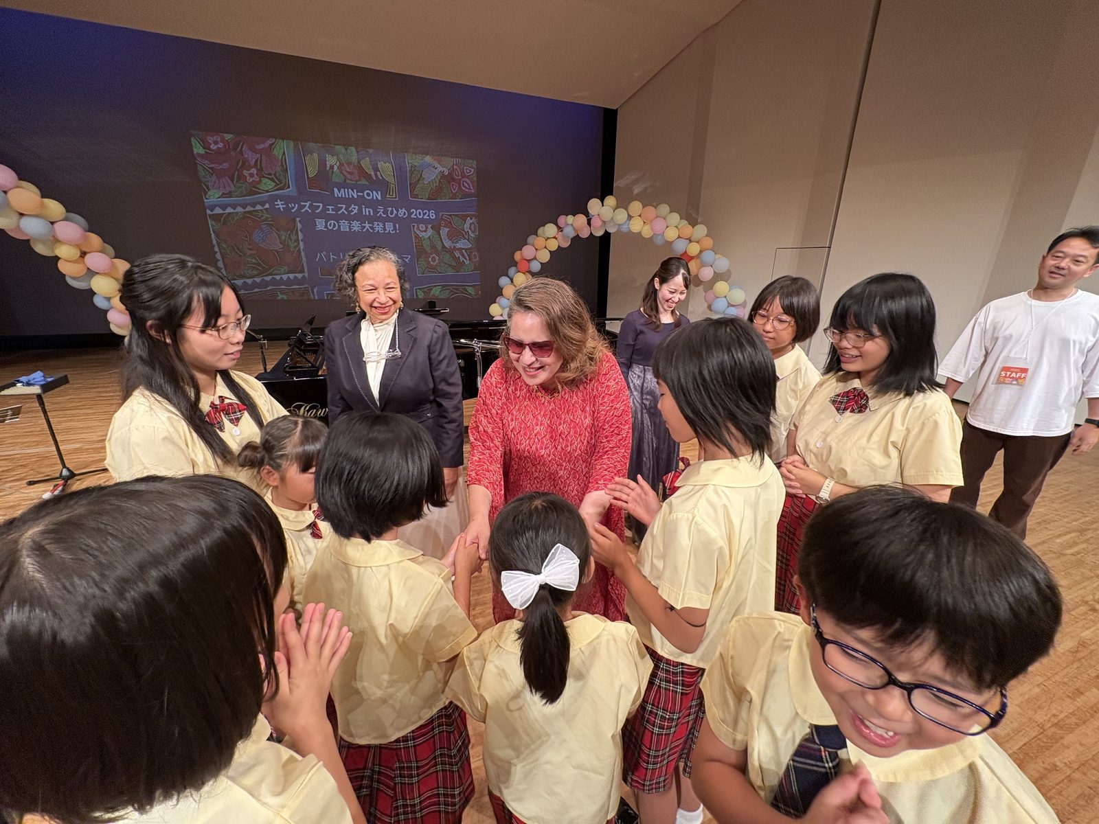 Patricia Vlieg and Vilma Esquivel greeting choir members in a close circle on stage